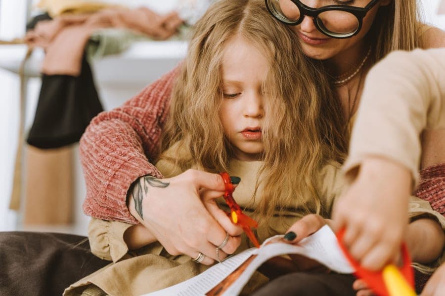 A child sewing at a table with an adult helping
